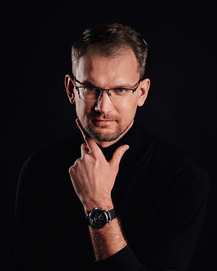 Marcin Dobrzyński with his hand at his chin, portrait against a dark background